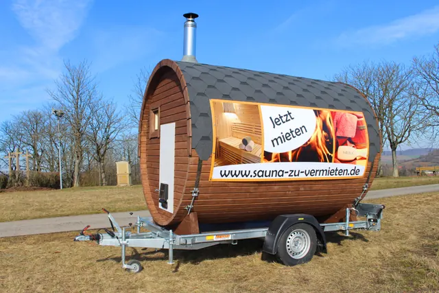 Fass-Sauna auf dem Anhänger auf einer Wiese unter blauem Himmel